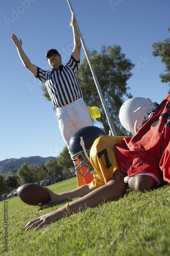 Photo: referee signalling touchdown over football player tackled in end zone referee signalling touchdown over football player tackled in end zone