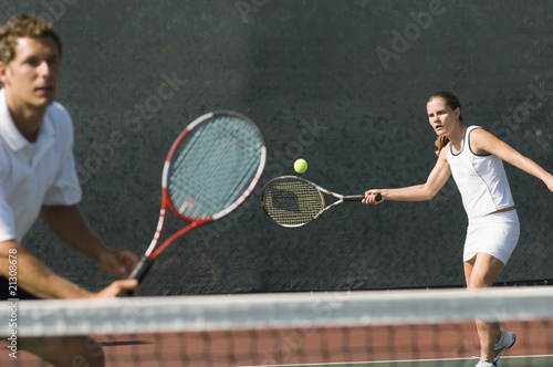 Photo: mixed doubles player hitting tennis ball partner standing near net mixed doubles player hitting tennis ball partner standing near net