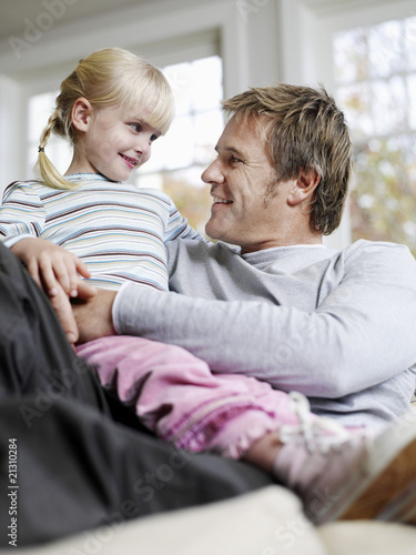 Photo: girl (3-4) sitting in father's lap in house girl (3-4) sitting in father's lap in house