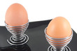 two eggs in holders on black plate isolated on white