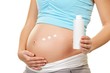 Pregnant woman applying cream to her belly .