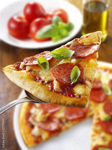 Photo: Slice of pepperoni pizza with basil on server Slice of pepperoni pizza with basil on server