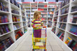 girl in bookshop, with cart for goods. There is one among racks.
