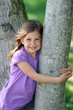 Cute young girl smiling and hugging a tree