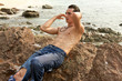 Muscular man running fingers through his wet hair on a beach.