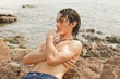 Young man resting on ocean rocks, hair wet from swimming.