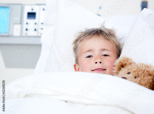 Photo: Sick adorable little boy lying in a hospital bed with his teddy Sick adorable little boy lying in a hospital bed with his teddy