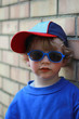 Junge mit Baseballcap und Sonnenbrille lehnt an Mauer