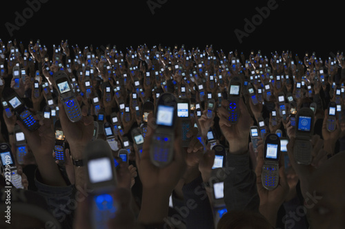 Photo: Large group of people holding open cell phones up in air Large group of people holding open cell phones up in air
