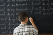 Rear view of boy writing on blackboard