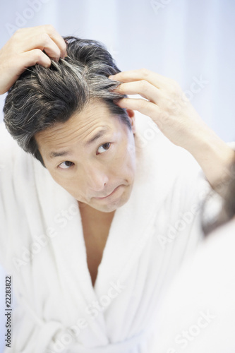 Photo: Asian man looking at gray hair in mirror Asian man looking at gray hair in mirror