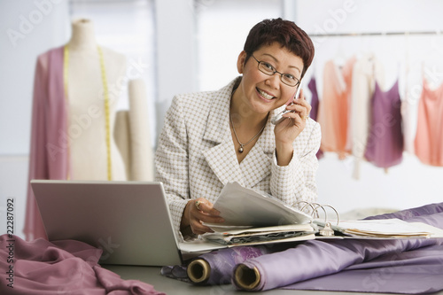 Photo: Asian female clothing designer talking on cell phone Asian female clothing designer talking on cell phone