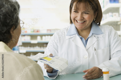 Photo: Hispanic female pharmacist handing medication to customer Hispanic female pharmacist handing medication to customer