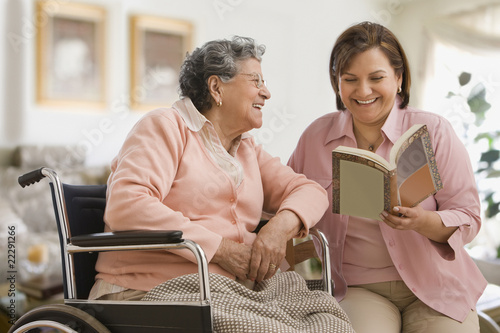 Photo: Hispanic woman reading to mother Hispanic woman reading to mother