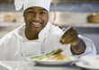 African male chef garnishing plate of food