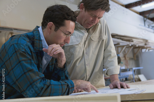 Photo: Multi-ethnic men looking paperwork in wood shop Multi-ethnic men looking paperwork in wood shop