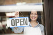 Hispanic woman hanging open sign on door