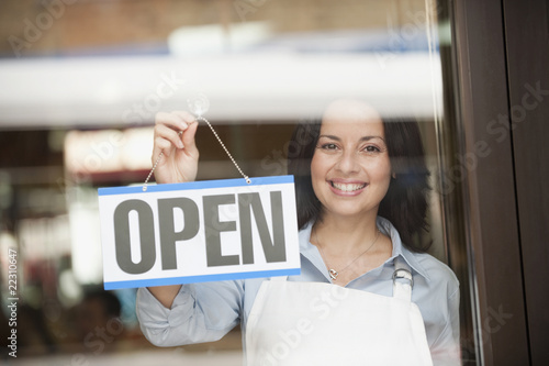 Foto: Hispanic woman hanging open sign on door Hispanic woman hanging open sign on door