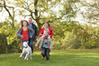 Foto: Young Family Outdoors Walking Through Park With Dog Young Family Outdoors Walking Through Park With Dog