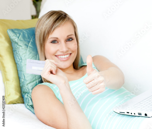 Cheerful woman shopping on-line lying on a sofa