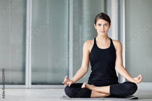 Photo: Cute young female practicing yoga on a mat in the lotus pose Cute young female practicing yoga on a mat in the lotus pose