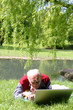 Alter Mann arbeitet mit dem Laptop im Grünen am Wasser