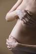 Pregnant woman stands with hand covering naked breast and stomach