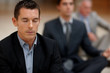Young business man meditating with colleagues at the back