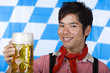 Lachender Chinese in Lederhose hält Oktoberfest Bierkrug (Mass)