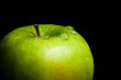 A wet green apple on black background (close-up)