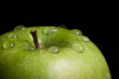 A wet green apple on black background (close-up)
