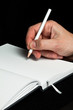 A male hand writing with a pencil in a blank book