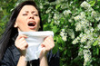 allergy to pollen: young woman sneezing among flowers