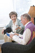 Senior couple chatting in living room reading book Senior couple chatting in living room reading book