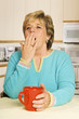 Yawning woman with red coffee mug in her kitchen Yawning woman with red coffee mug in her kitchen