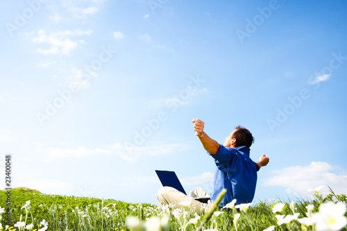 Photo: Man working with laptop in a meadow of flowers with copyspace Man working with laptop in a meadow of flowers with copyspace
