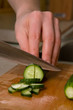 Hands of cook cutting cucumber.