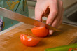 Hands of cook cutting tomato.
