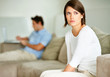 Upset young woman sitting with her husband in background