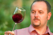 Young man is tasting red wine in the vineyard at sunset