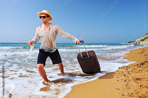 Photo: A tourist carrying a suitcase at the beach at Corfu island A tourist carrying a suitcase at the beach at Corfu island