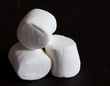 Three white marshmallows on a black background