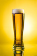 Glass of beer close-up with froth over yellow background