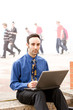 Man sitting on steps with laptop, people passing by