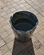Old rusty bucket with water on grey sidewalk