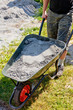 Somebody pushing the wheelbarrow full of grey sand Somebody pushing the wheelbarrow full of grey sand