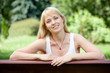 Young cheerful blond woman on the bench in summer park