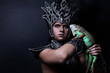 Young pagan priest in ritual suit with green iguana in his hands