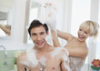 Woman playing with soap suds on man in bathroom