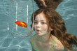 Photo: girl making funny fish face swimming underwater with goldfish girl making funny fish face swimming underwater with goldfish